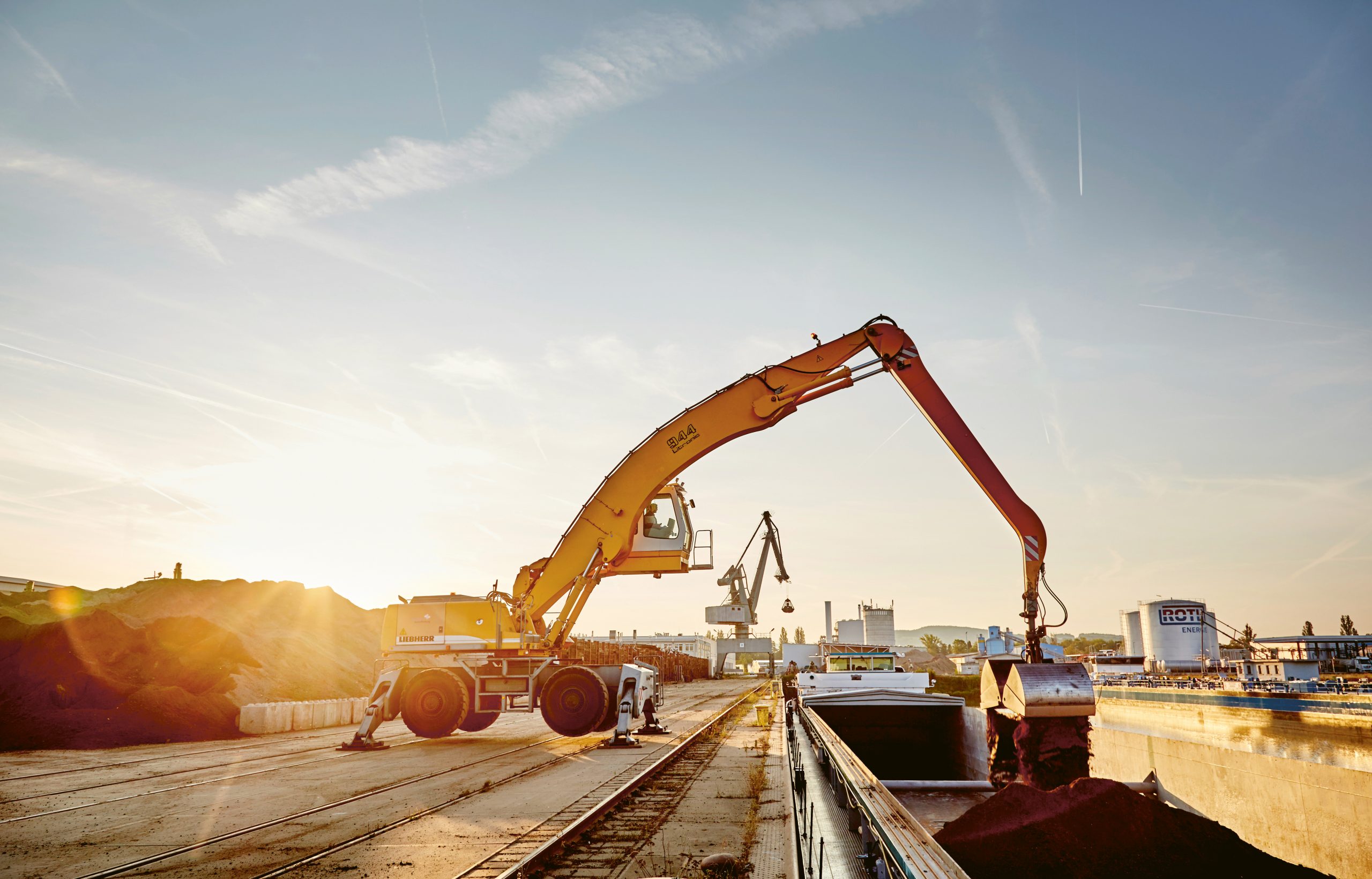 Blasius Schuster Bayern/Aschaffenburg S. 66-69 Materialumschlagbagger verlädt mineralische Baustoffe im Gegenlicht der Abendsonne auf ein Binnenschiff am Hafen